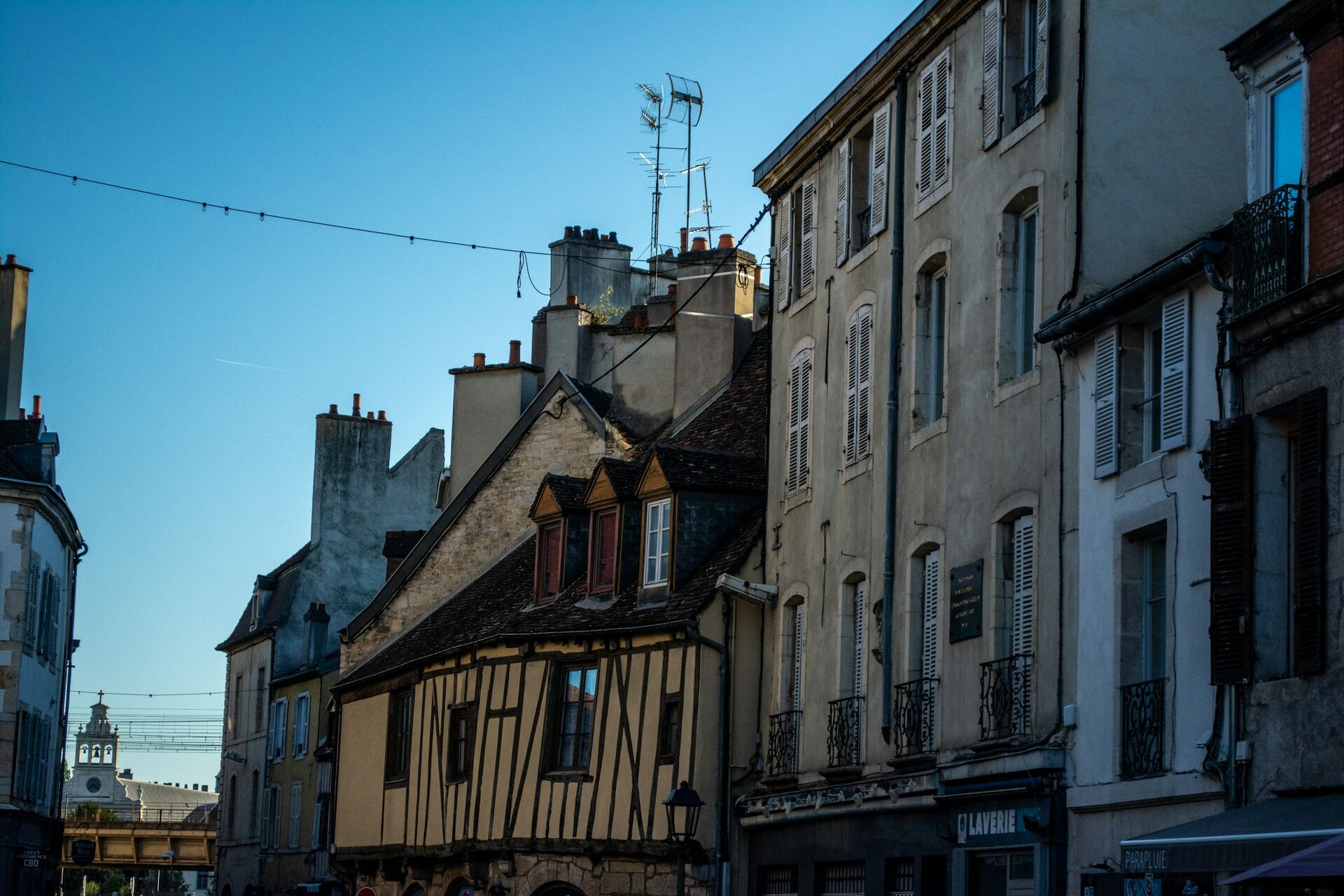 Rue d’une ville française aux façades réchauffées par le soleil, volets fermés contre la chaleur