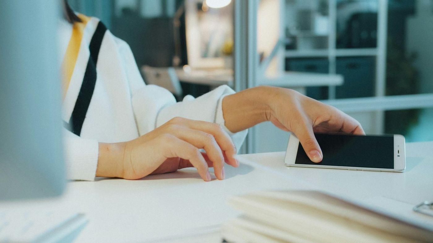 À un bureau, la main d’une personne posée sur un téléphone, des dossiers au premier plan.